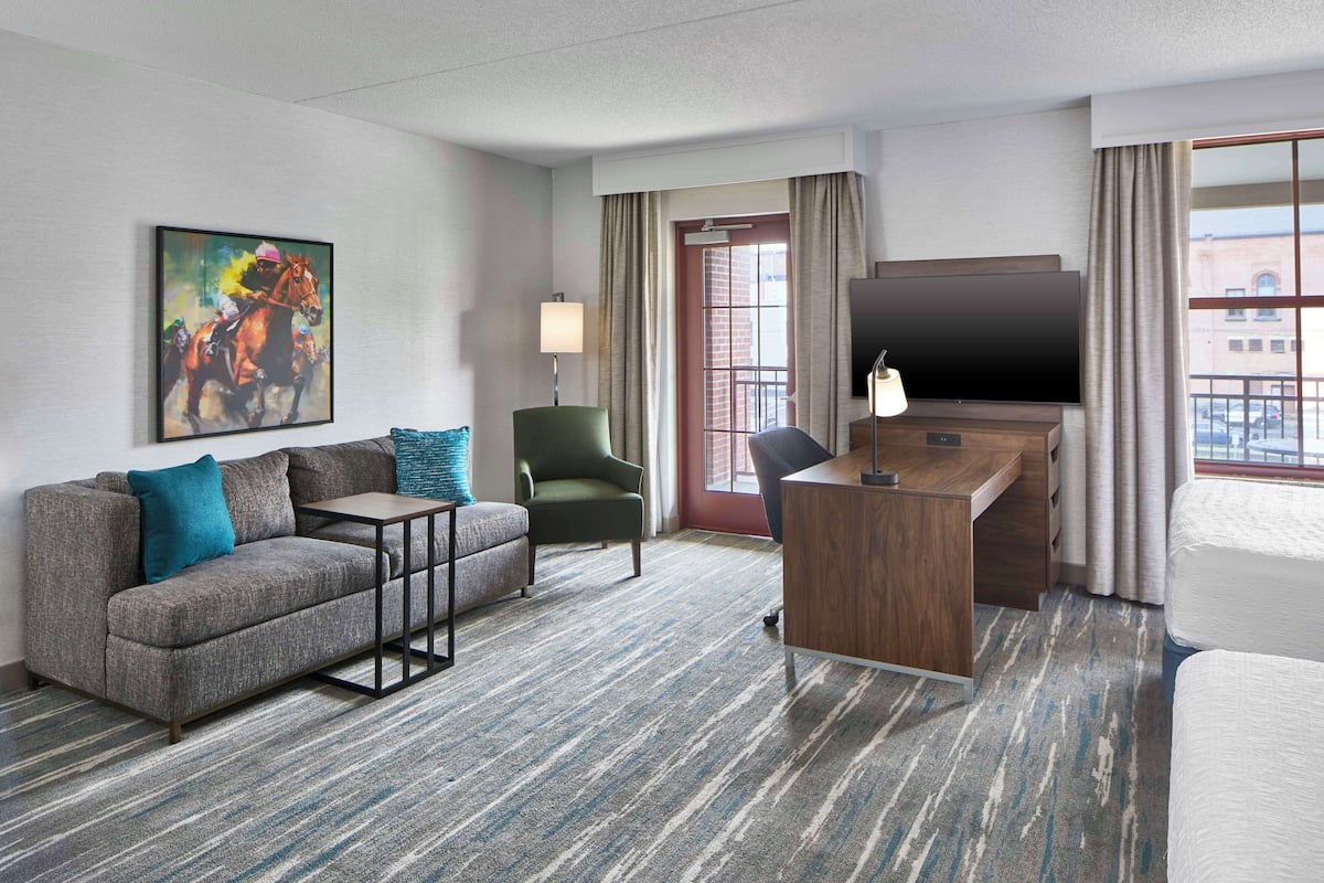 A hotel room with a sofa, armchair, desk, and TV.