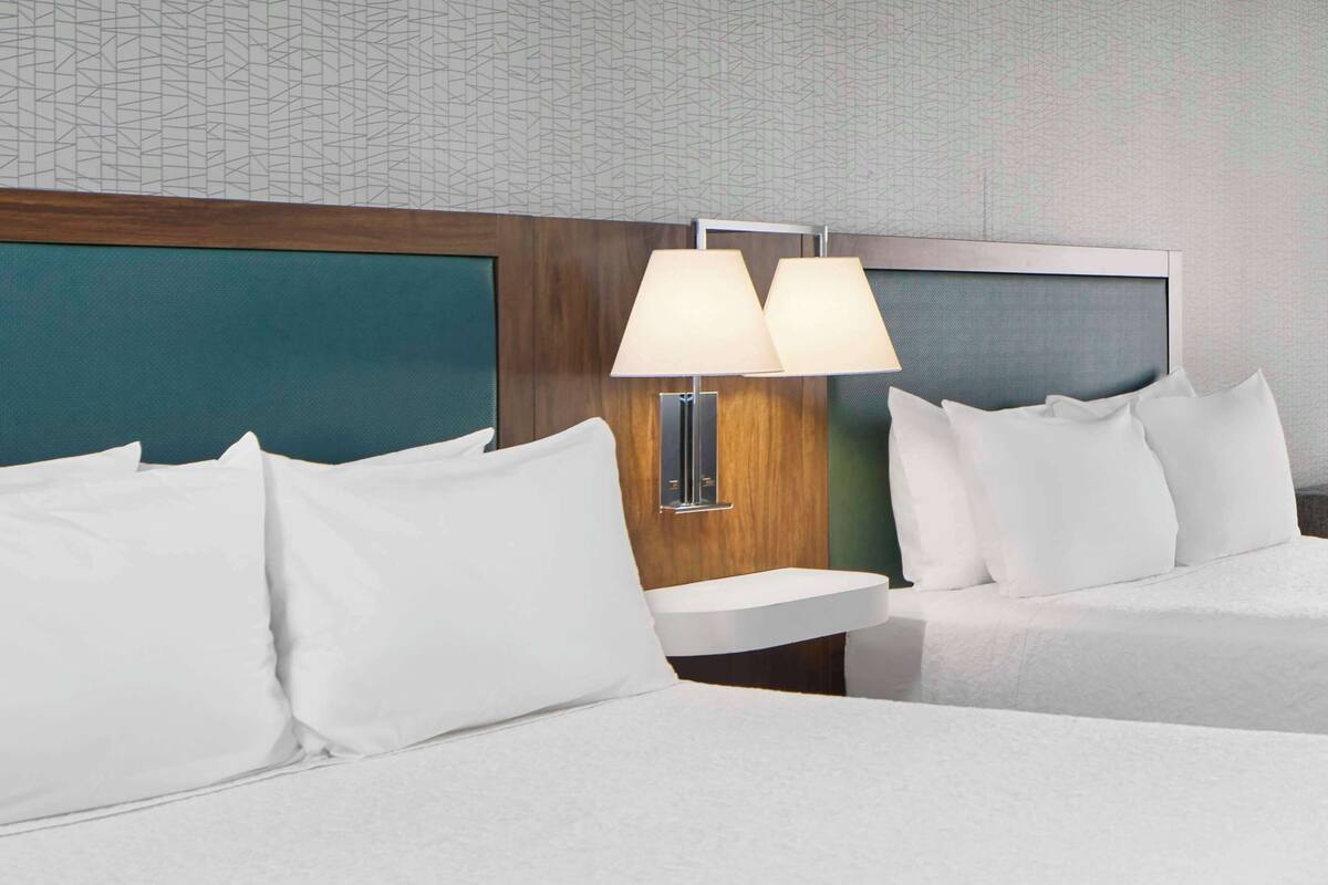 A hotel room with two beds, a wooden headboard, a nightstand with a lamp, and a wall with a geometric pattern.