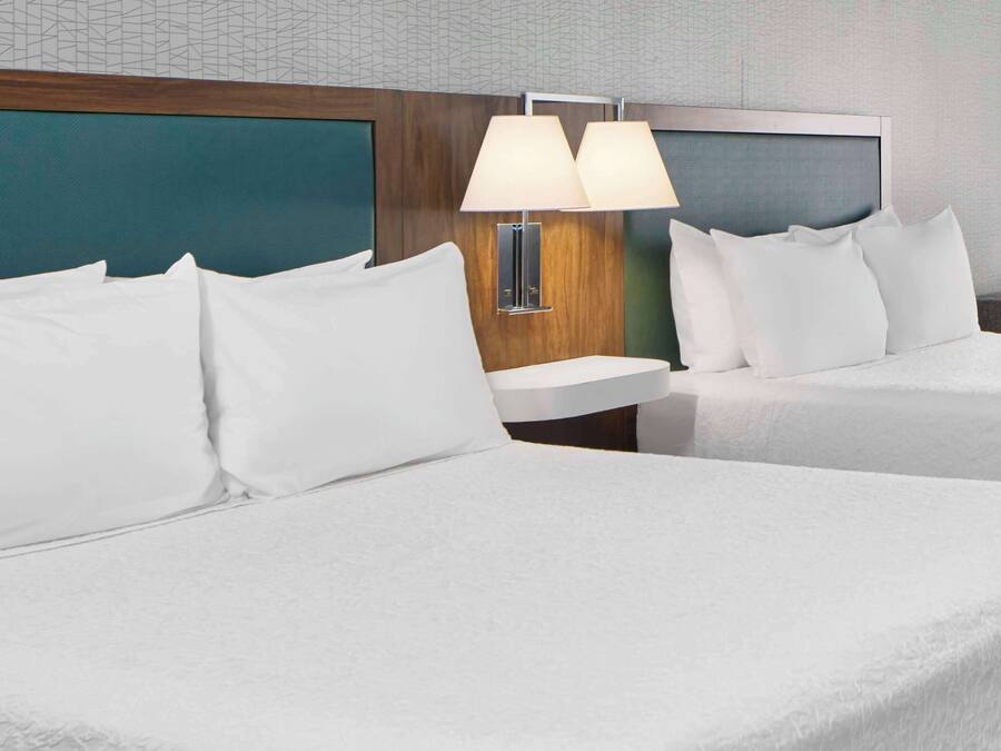 A hotel room with two beds, a wooden headboard, a nightstand with a lamp, and a wall with a geometric pattern.