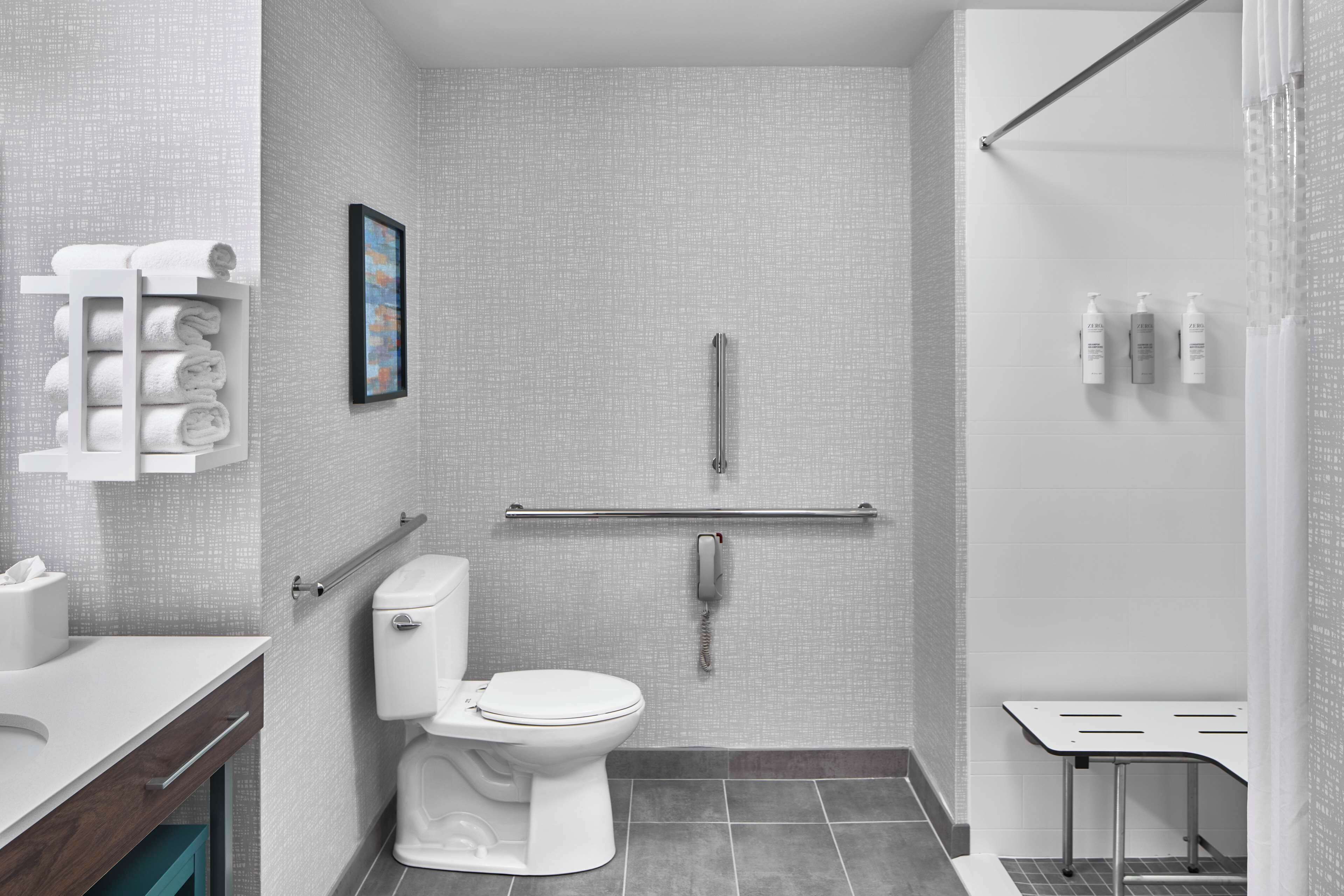 A modern bathroom with a toilet, a handrail, a towel rack, and a shower area.