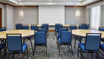 A conference room with multiple tables and chairs, a projector screen, and a carpeted floor.
