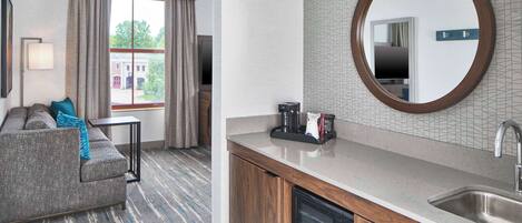 Habitación de hotel con sofá, una mesita, microondas, lavabo y un espejo grande.