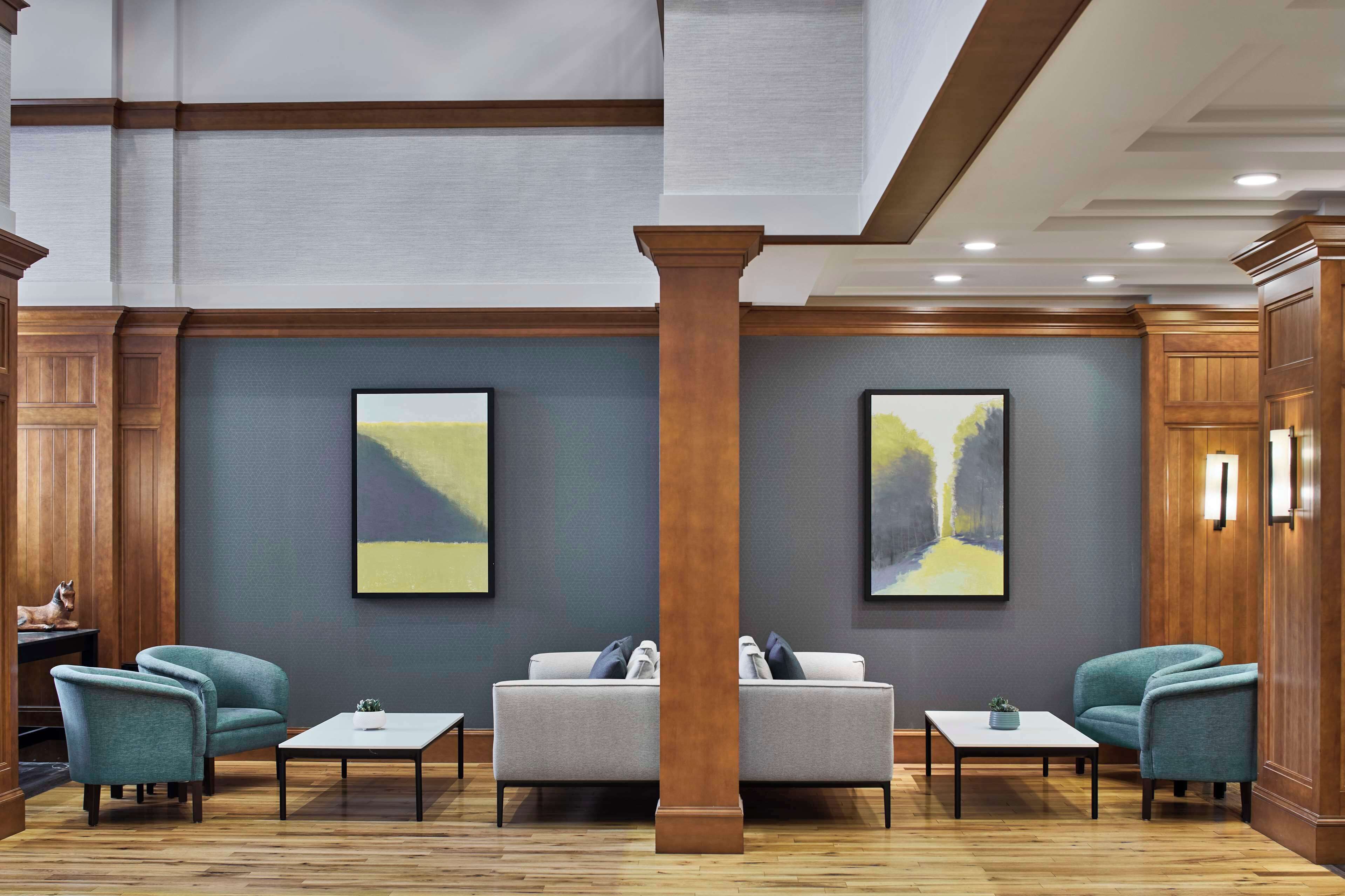 A lobby with a grey sofa, teal armchairs, a wooden column, and abstract paintings on the wall.