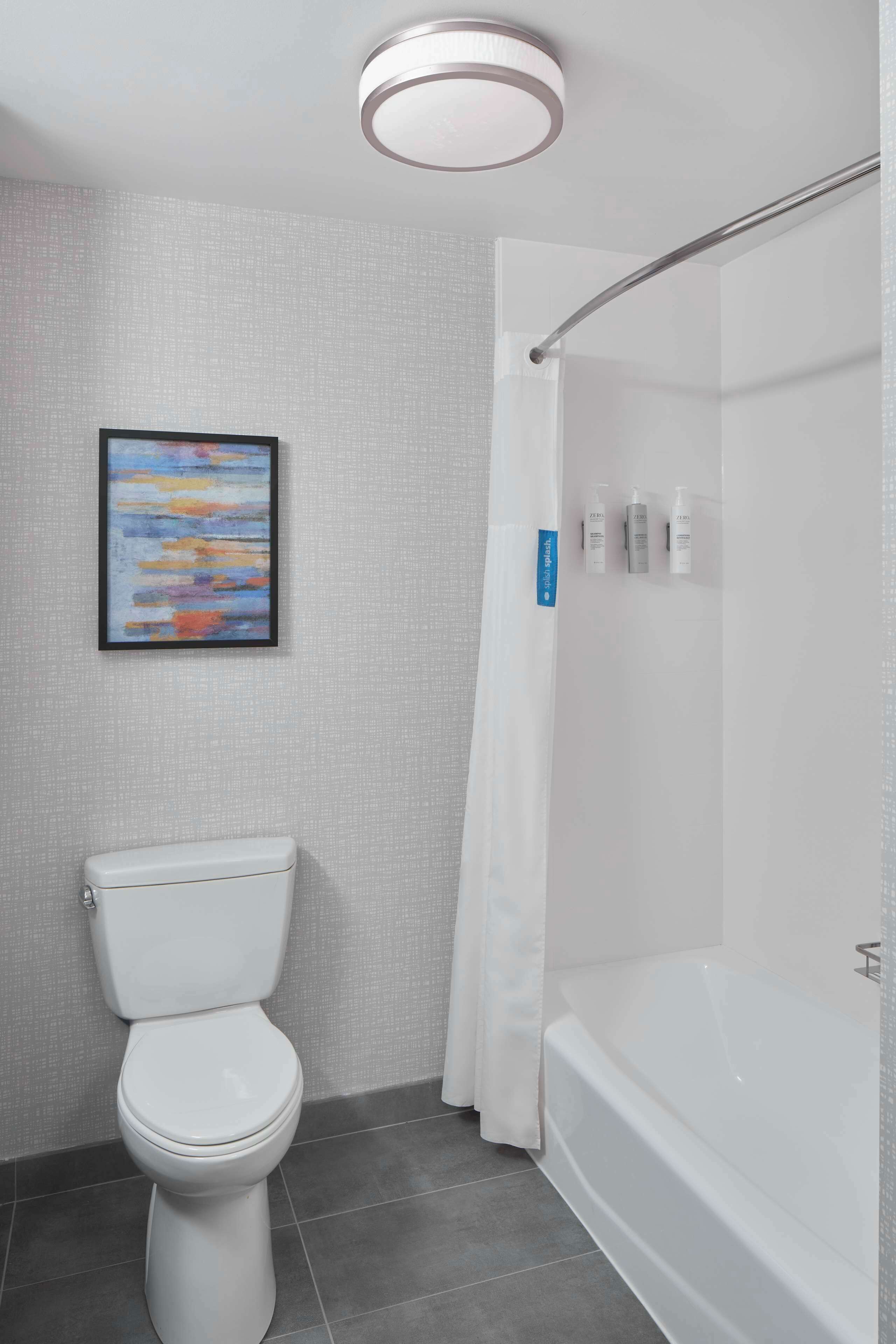 A modern bathroom with a toilet, a shower with a glass door, and a framed abstract painting on the wall.