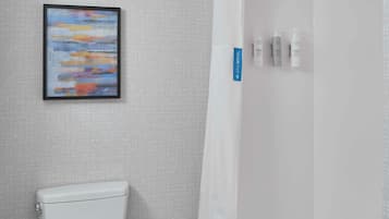 A modern bathroom with a toilet, a shower with a glass door, and a framed abstract painting on the wall.