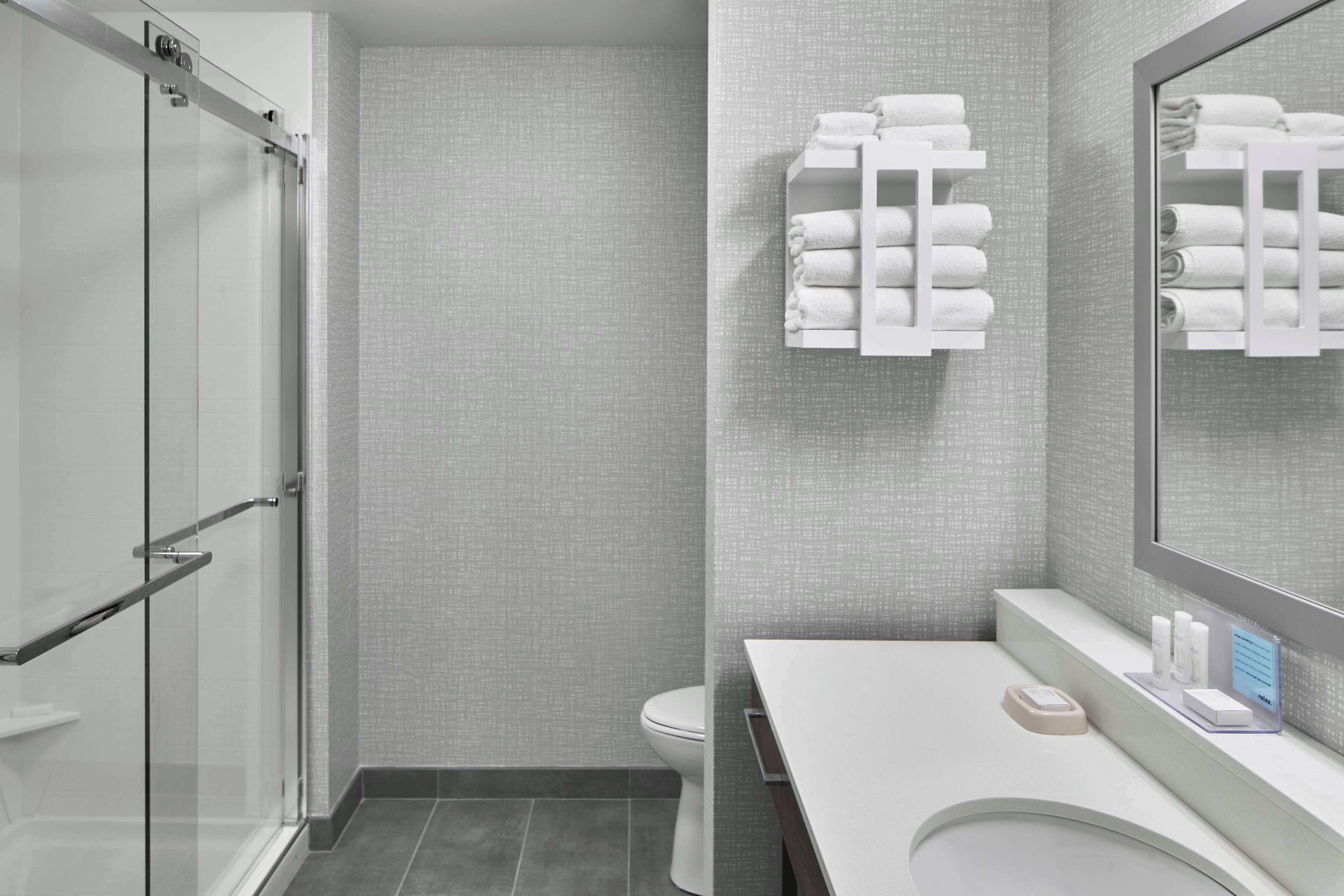 Een moderne badkamer met een douchecabine van glas, een toilet en een wastafel met spiegel en handdoekhouder.