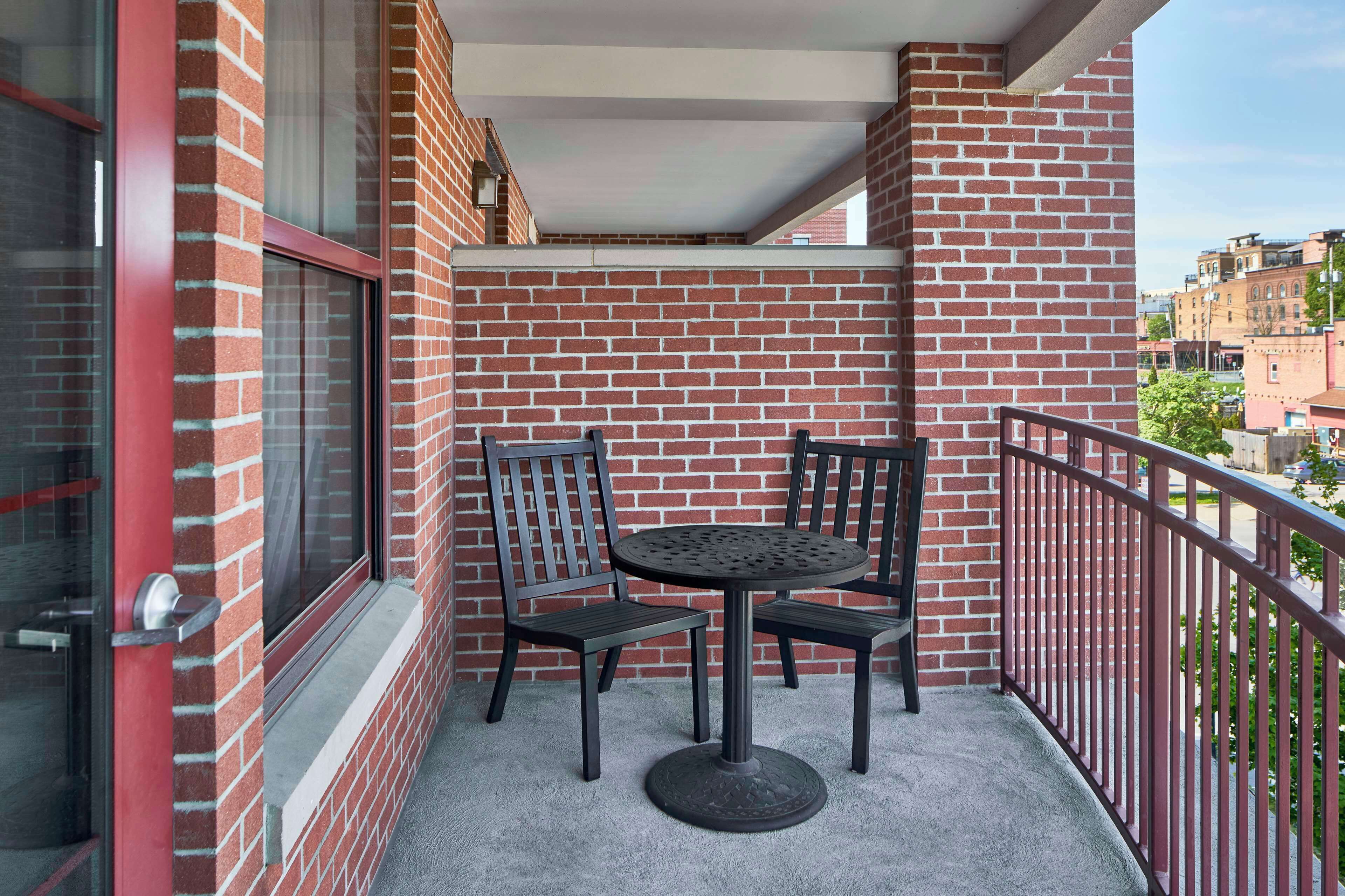 A balcony with a brick wall, a round table with chairs, and a metal railing.