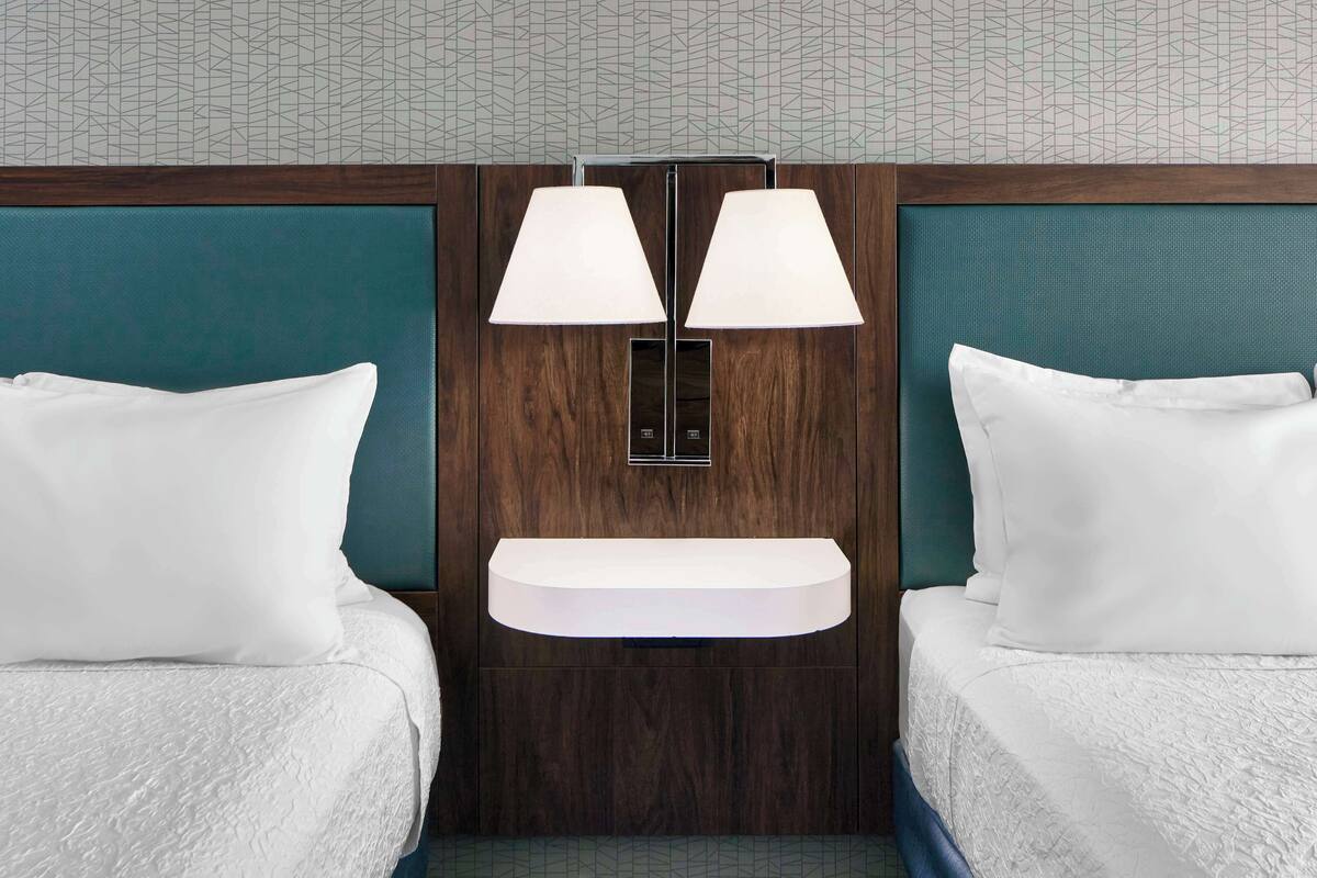 A hotel room with two beds, a built-in shelf, and a wall-mounted lamp.