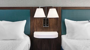 Quarto de hotel com duas camas, prateleira embutida e luminária na parede.