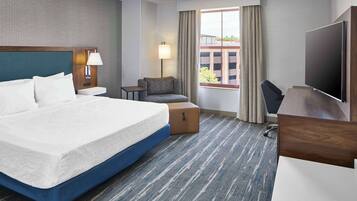 A hotel room with a large bed, a desk, a chair, a TV, a lamp, and a window with curtains.