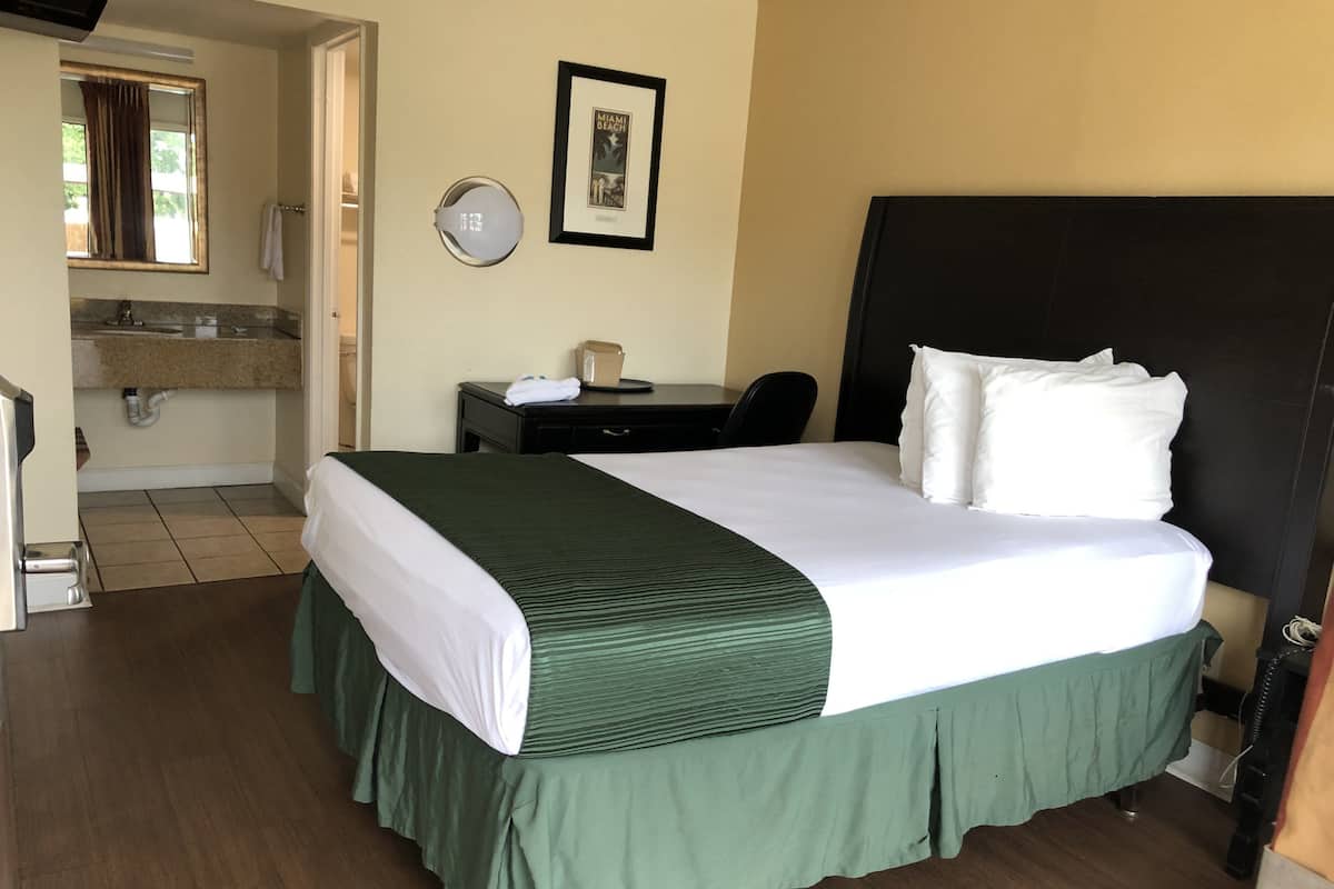 Ein Hotelzimmer mit Bett, Schreibtisch, Stuhl, Bad und einem gerahmten Bild an der Wand.