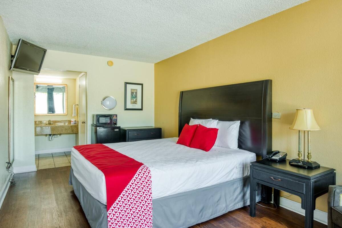 Ein Hotelzimmer mit Bett, Nachttisch, Lampe und einem an der Wand befestigten Fernseher.