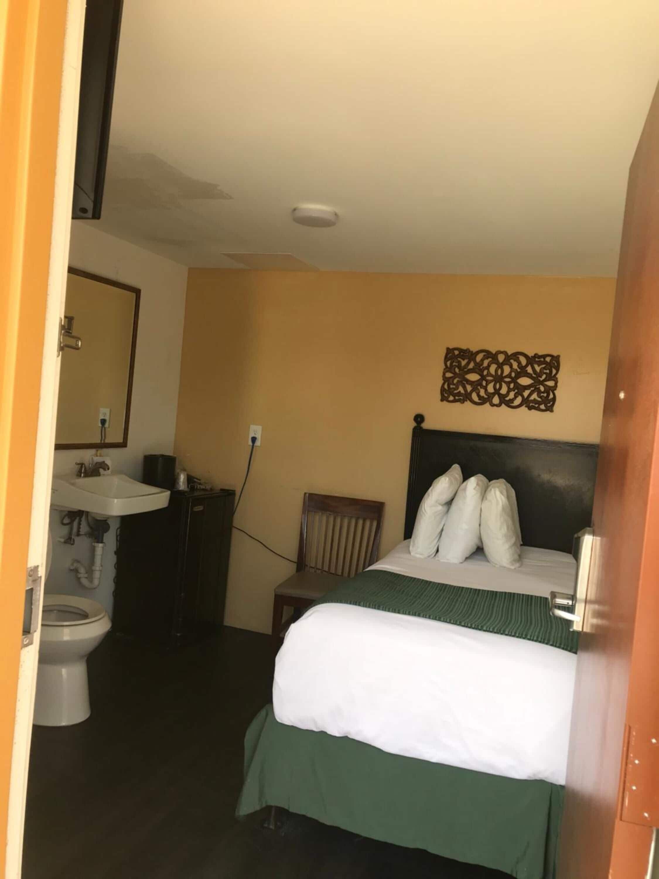 A hotel room with a bed, a chair, a sink, and a toilet.