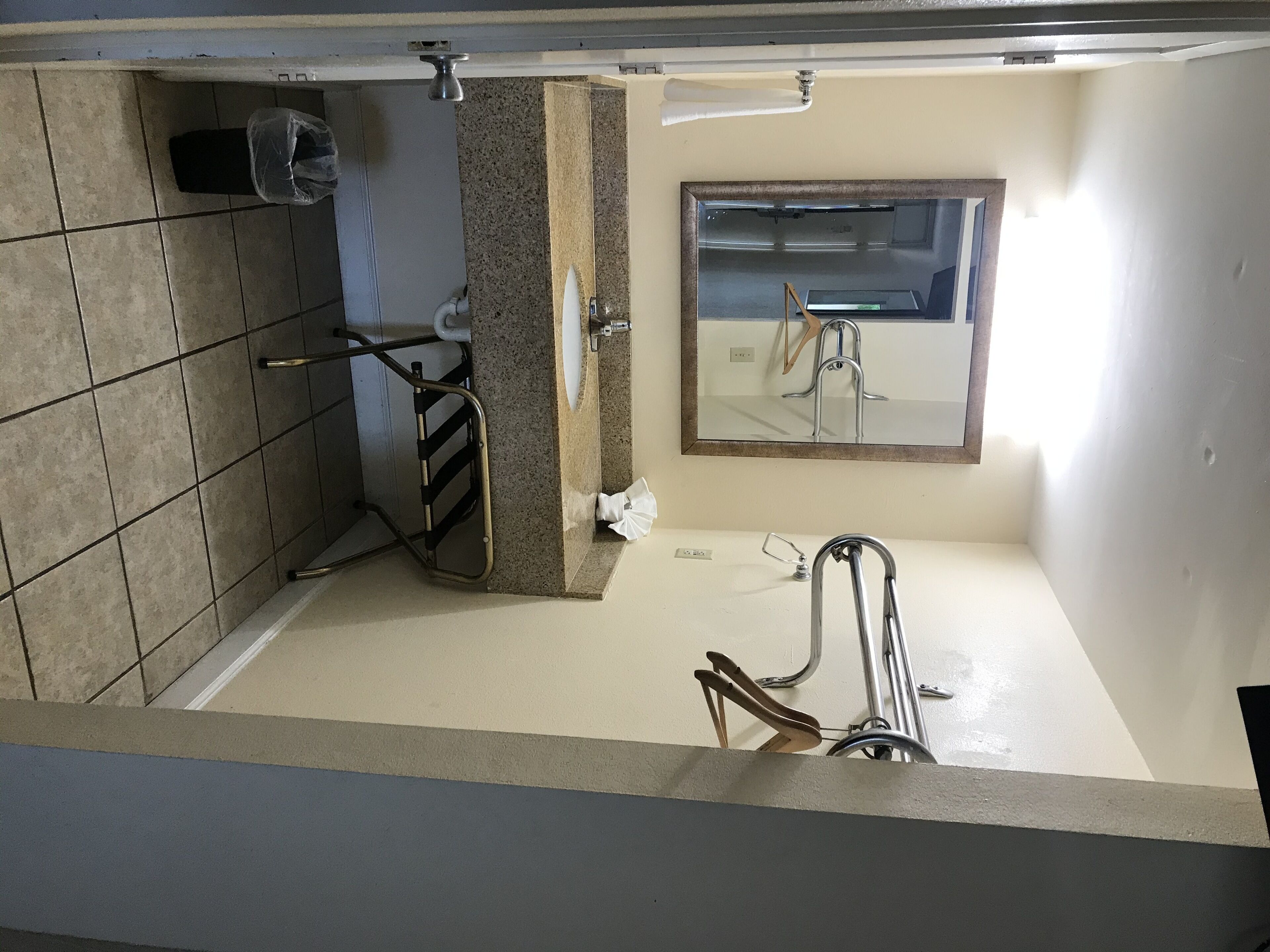 Une salle de bain avec un sol carrelé, un lavabo avec un miroir, un porte-serviettes et une barre d’appui.