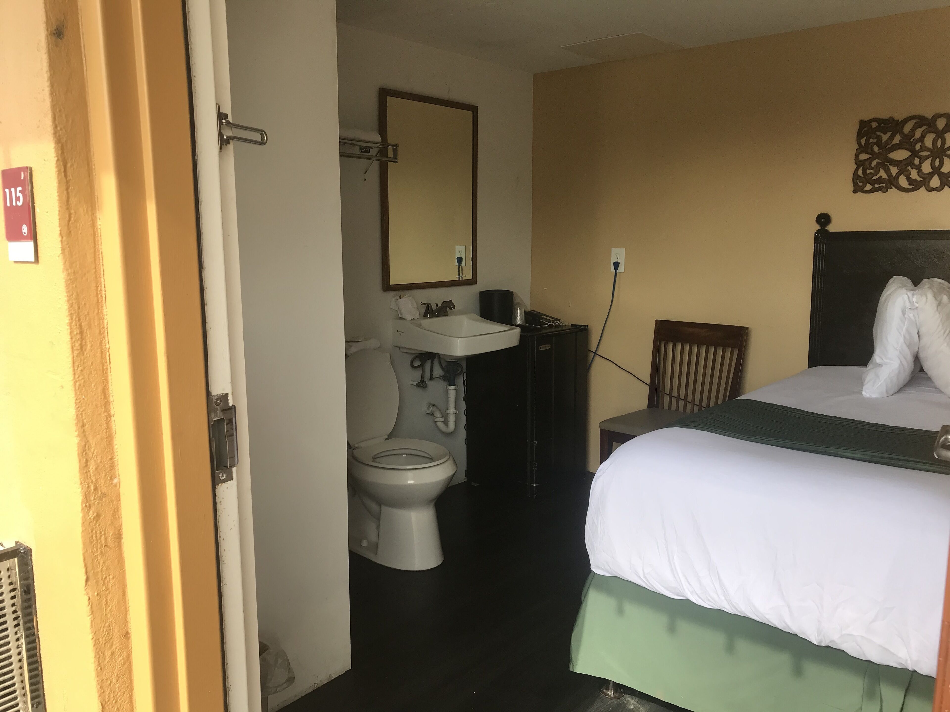 Hotellihuone, jossa on sänky, puinen tuoli, pesuallas ja wc.