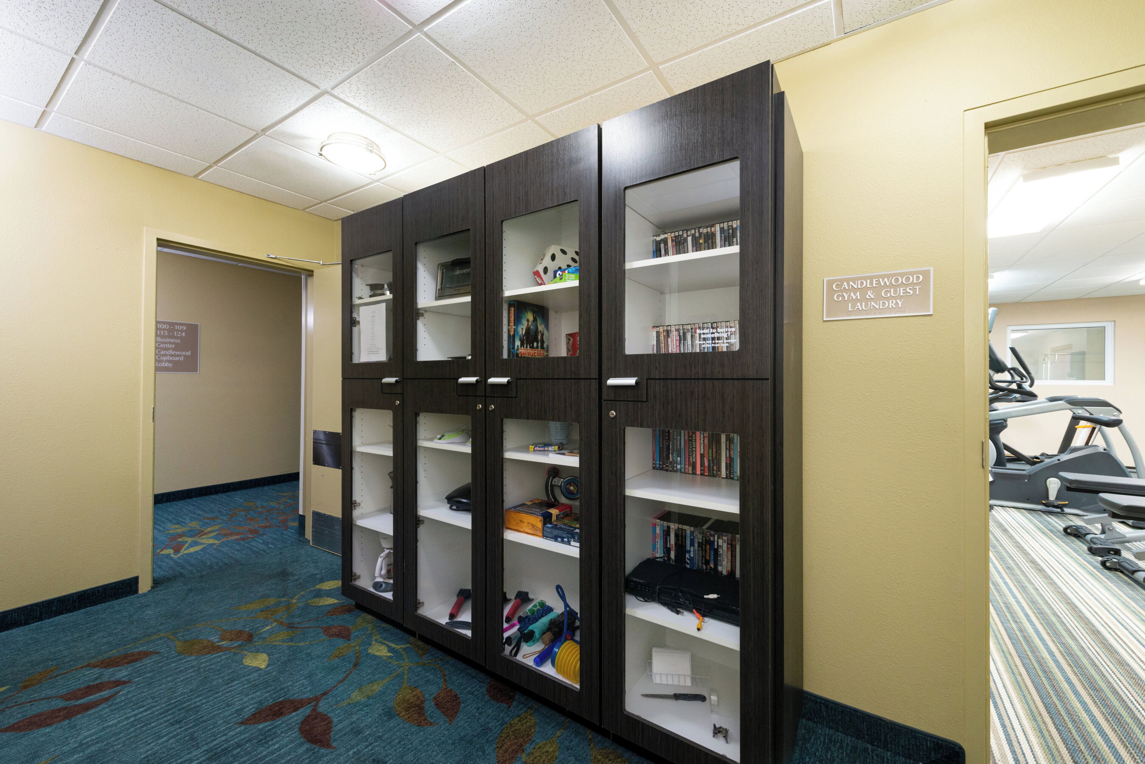 A hotel lobby with a large wooden bookcase, a treadmill, and a sign indicating a gym and guest laundry.