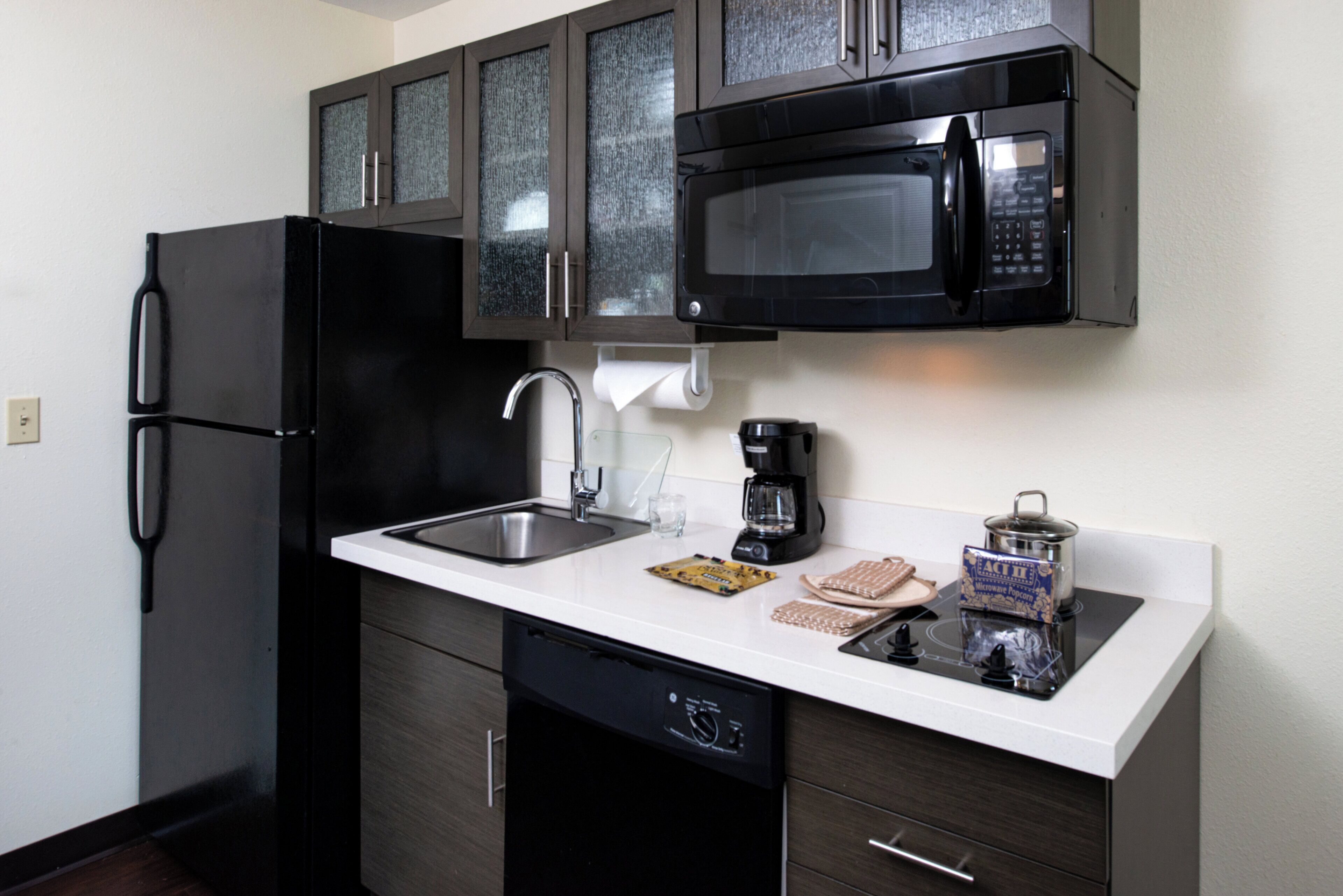 A compact kitchen with a black refrigerator, a microwave, a coffee maker, and a dishwasher.