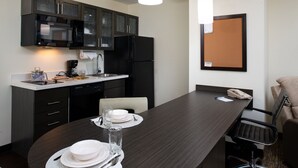Een moderne keuken met donkere kastjes, een zwarte koelkast en een eethoek met een donker houten tafel gedekt voor twee personen.