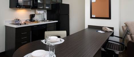 Une cuisine moderne avec des meubles de couleur sombre, un réfrigérateur noir et un coin repas doté d’une table en bois foncé, mise pour deux personnes.