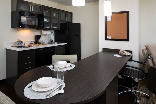 Une cuisine moderne avec des meubles de couleur sombre, un réfrigérateur noir et un coin repas doté d’une table en bois foncé, mise pour deux personnes.