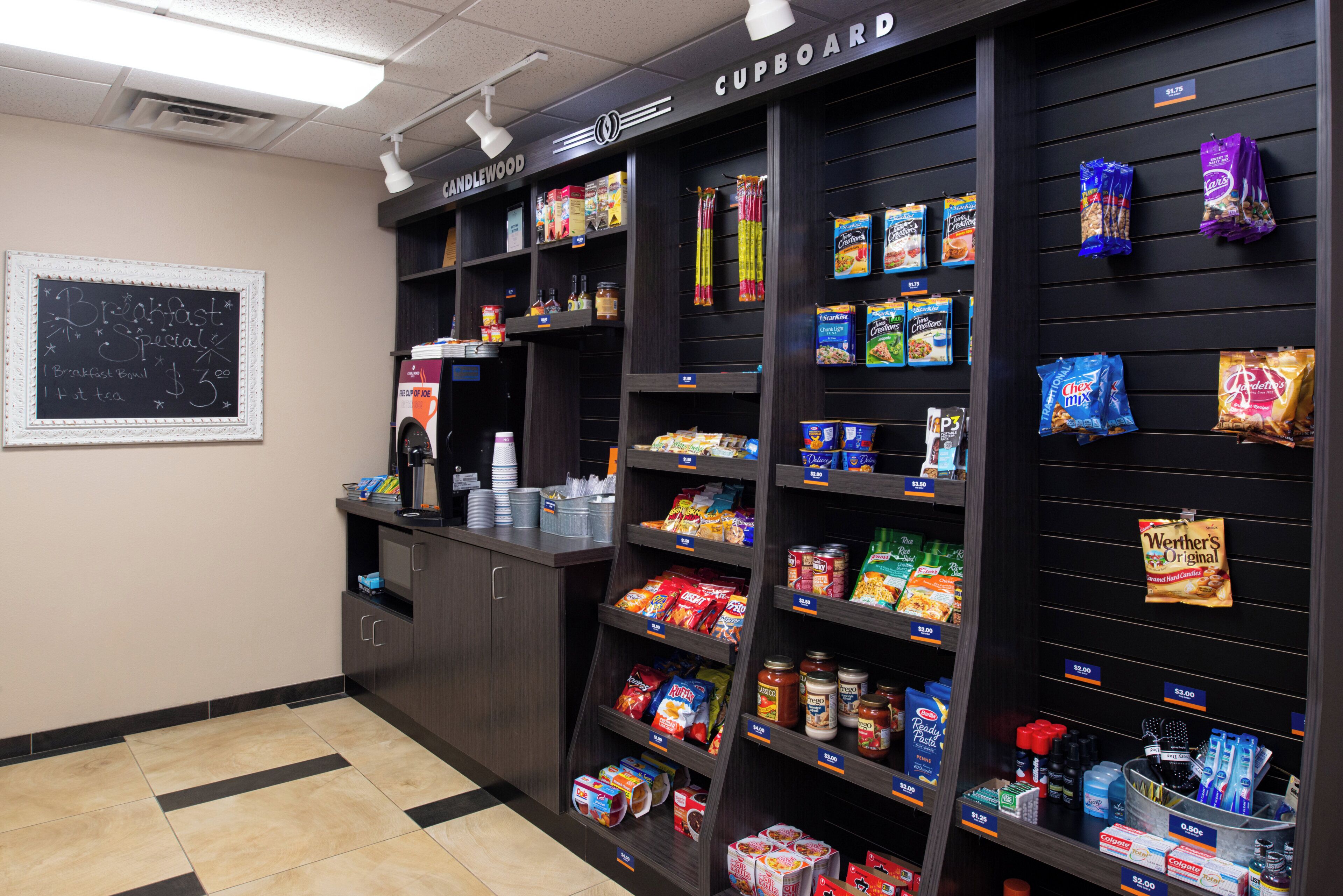 A kitchenette area with a coffee machine, a chalkboard menu, and shelves stocked with snacks and condiments.