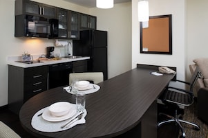 Una cocina moderna con armarios oscuros, un microondas y un refrigerador. Hay una mesa de comedor preparada con platos, vasos y cubiertos.
