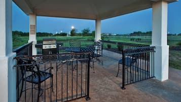 Un patio al aire libre con una parrilla y zona de estar, rodeado por una valla metálica.