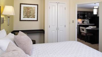 A hotel room with a bed, pillows, a nightstand, a wall-mounted lamp, a framed picture, a closet, and a kitchenette.