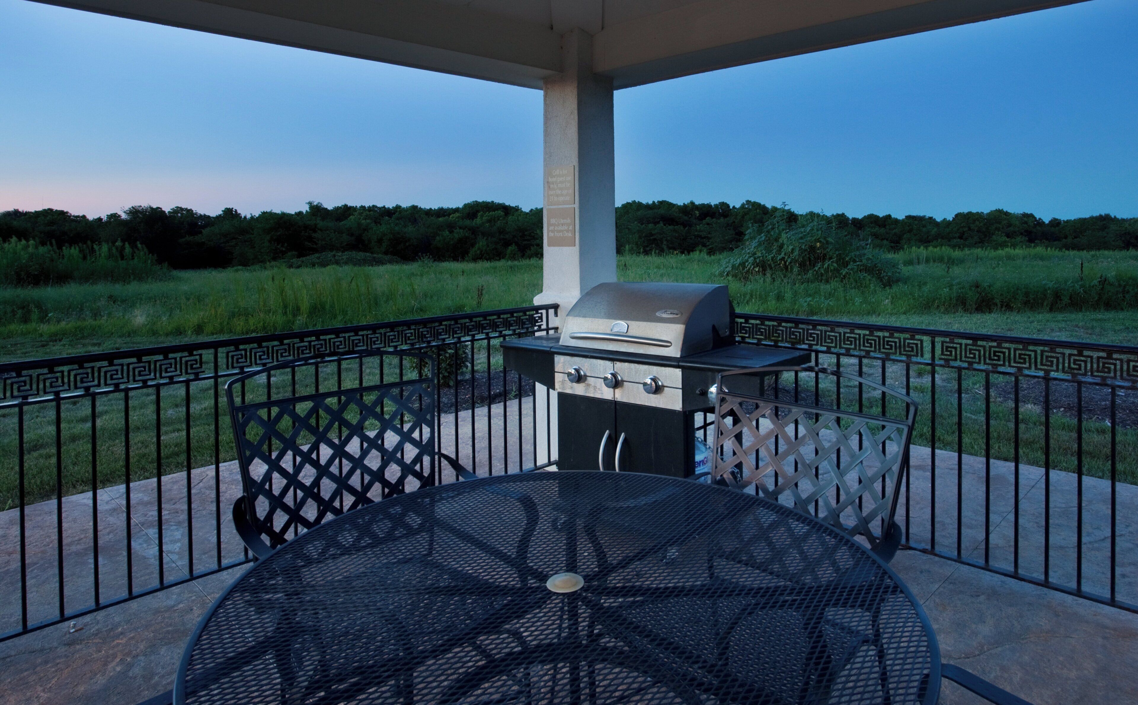 Un patio al aire libre con una parrilla, una mesa y vistas a un campo cubierto de césped.