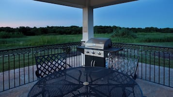 Un patio al aire libre con una parrilla, una mesa y vistas a un campo cubierto de césped.