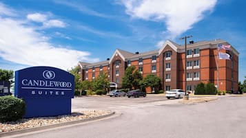Letrero de hotel con 'Candlewood Suites', un edificio de ladrillo con varias ventanas y una bandera.