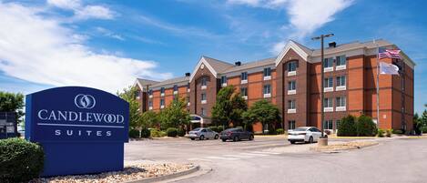A hotel sign with 'Candlewood Suites' and a brick building with multiple windows and a flag.