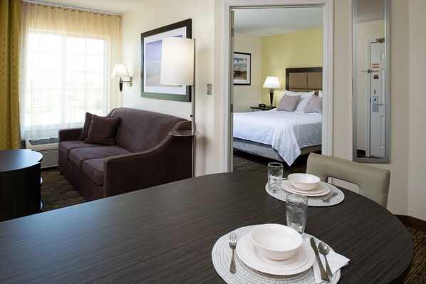 Ein Hotelzimmer mit Esstisch für zwei Personen, einer Couch, einem Bett und einem durchgegangenen Tür sichtbaren Badezimmer.