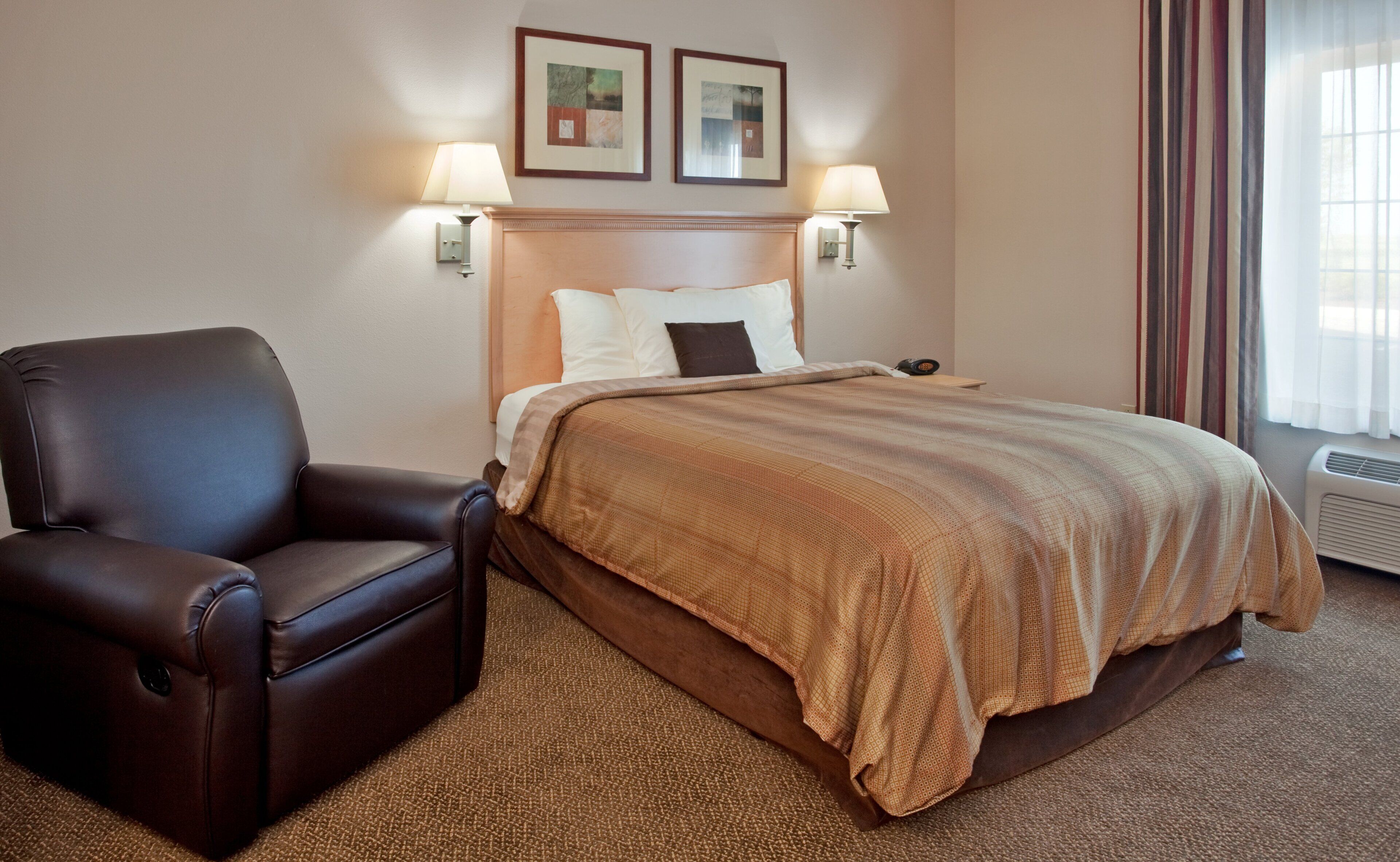 A hotel room with a bed, a chair, two wall-mounted lamps, and a window with curtains.