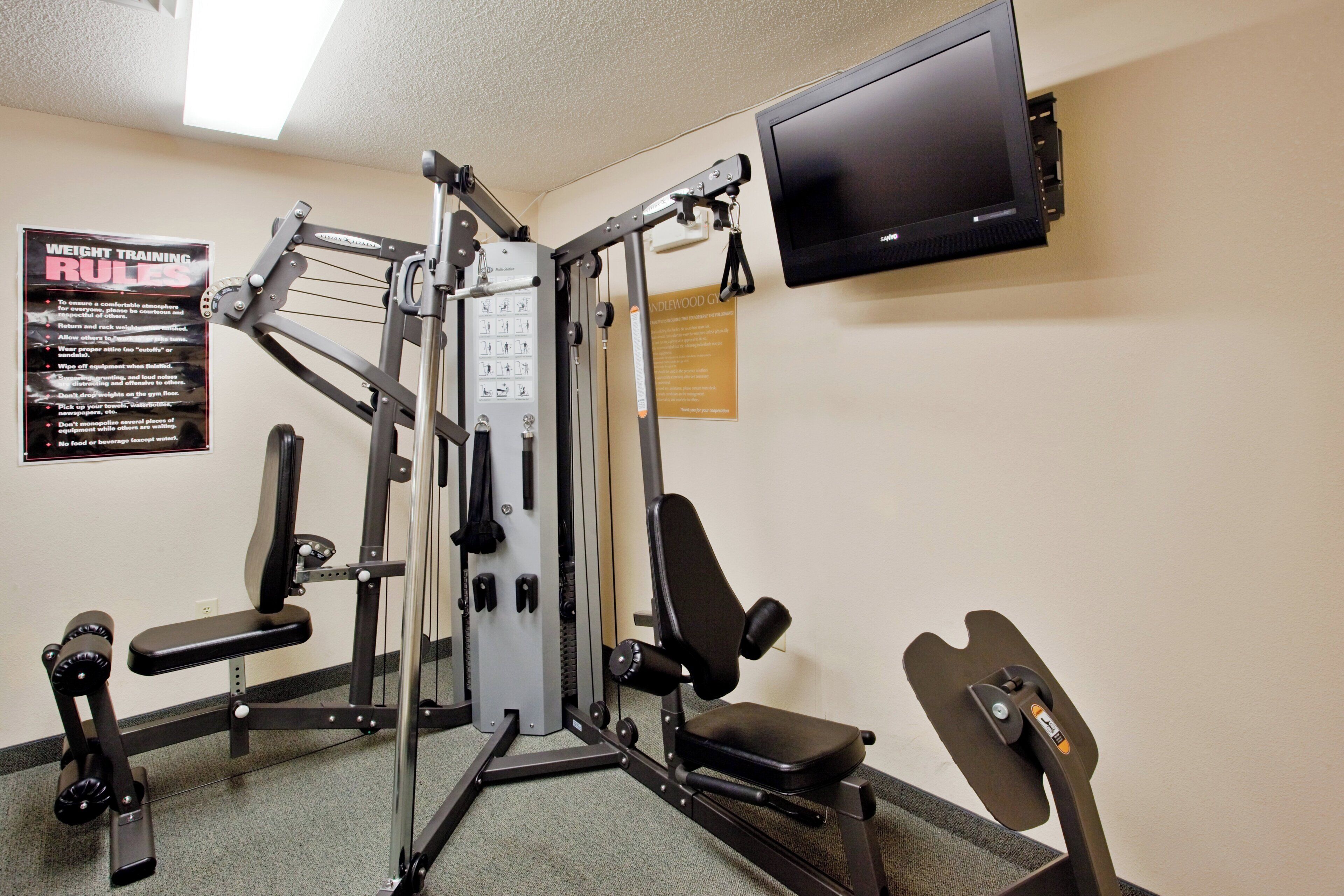 A gym with weight training equipment, a television, and a poster with rules.