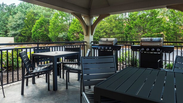 Une terrasse extérieure dotée d’un espace salon abrité, d’un barbecue et offrant une vue sur la verdure environnante.
