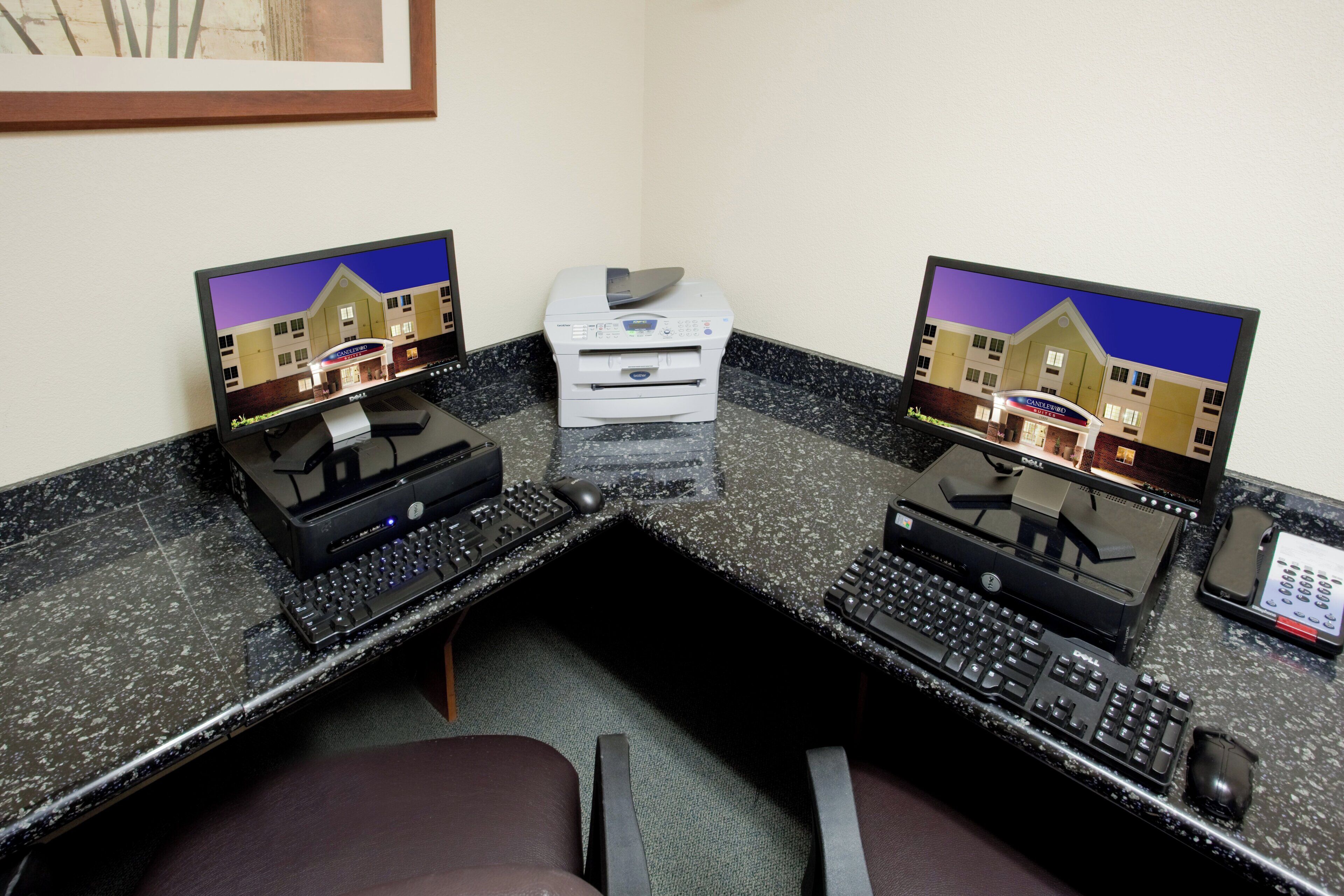 A hotel lobby with a reception desk, two computer workstations, a printer, and a telephone.