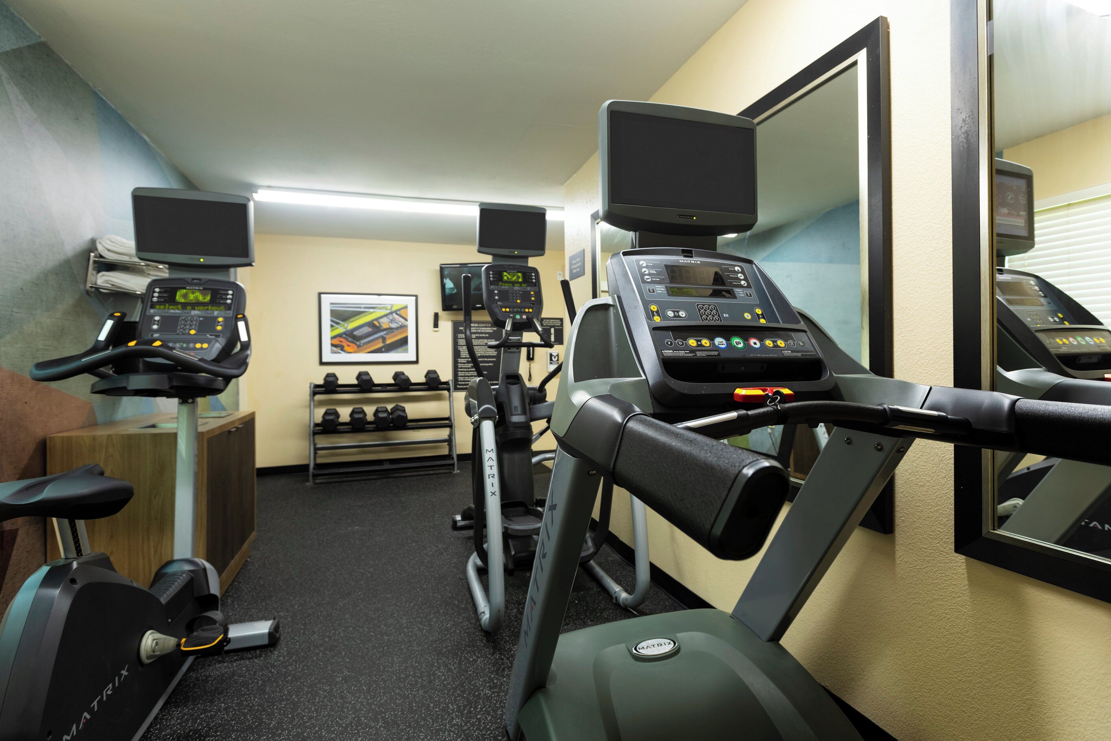 A gym with various exercise equipment, including treadmills and stationary bikes, and a mirror on the wall.