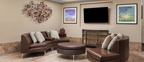 A modern living room with a sectional sofa, ottoman, flat-screen TV, fireplace, and wall art.
