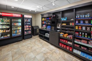A snack bar with refrigerated beverage dispensers, shelves stocked with snacks, and a counter area. - Candlewood Suites Omaha Airport by IHG (Omaha)