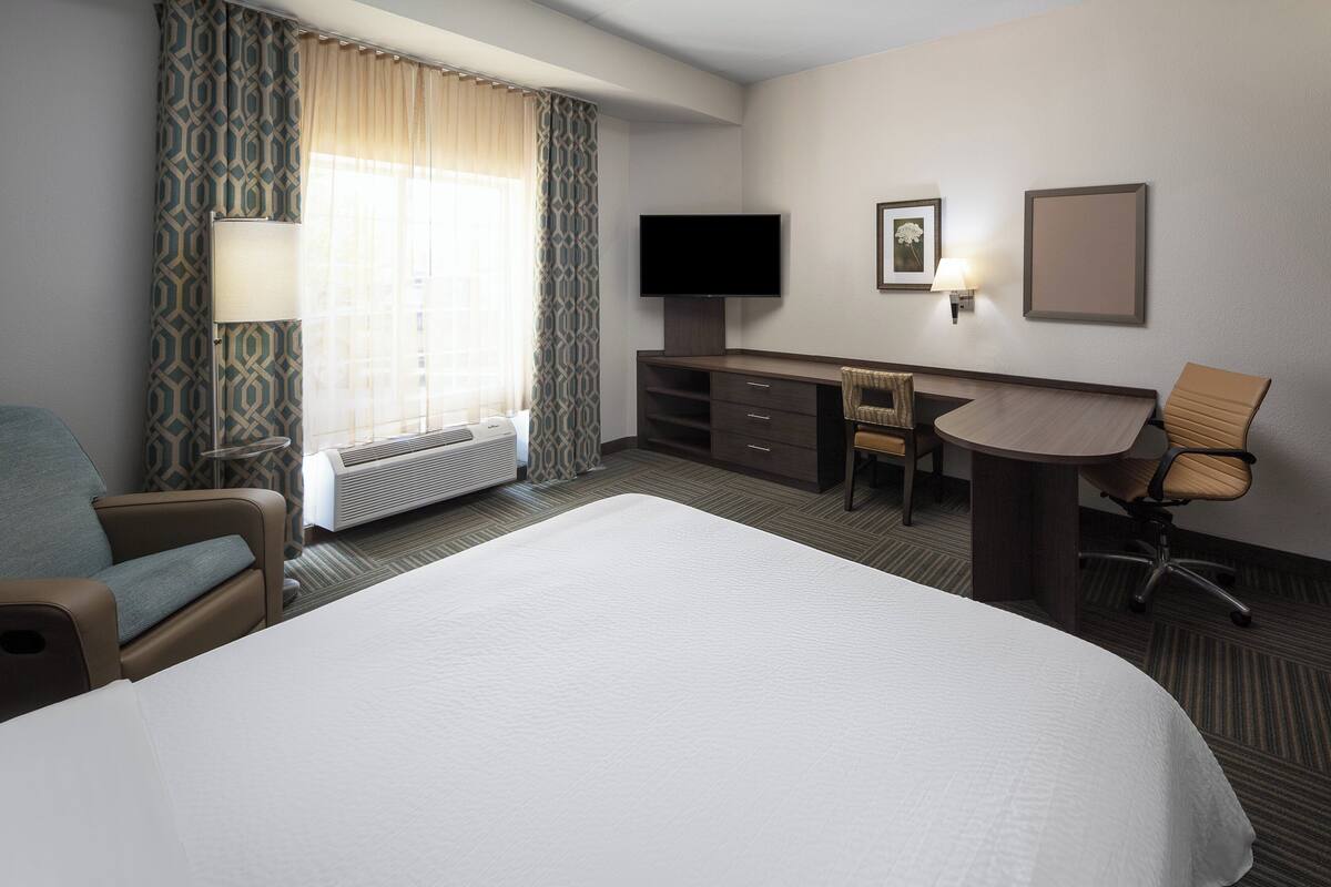 Una habitación de hotel con una cama grande, un escritorio con silla, un televisor y una ventana con cortinas.