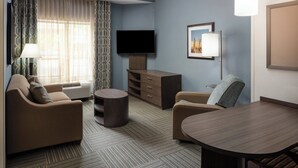 A hotel room with a sofa, armchair, dining table, TV, and a lamp.