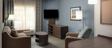 Een hotelkamer met een bank, fauteuil, eettafel, televisie en een lamp.