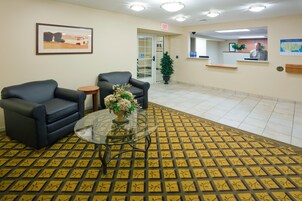 Un'area reception con due divani neri, un tavolino in vetro con un centrotavola floreale, una moquette decorata e una scrivania reception con una persona dietro.