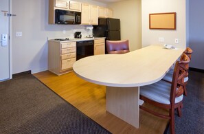 A compact kitchen with a dining area, featuring a microwave, refrigerator, and a small sink. - Candlewood Suites Milwaukee Brown Deer by IHG (Milwaukee)