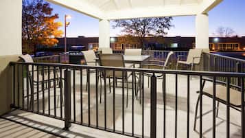 An outdoor patio area with tables and chairs, a railing, and a view of a parking lot and buildings in the background.