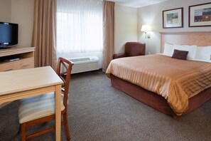 A hotel room with a bed, a desk, a chair, a television, and an air conditioning unit. - Candlewood Suites Milwaukee Brown Deer by IHG (Milwaukee)
