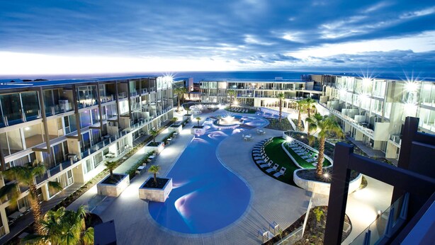 Een modern hotel met een zwembad, meerdere balkons en uitzicht op de oceaan.