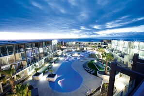 Un hotel moderno con zona de piscina, varios balcones y vistas al océano.