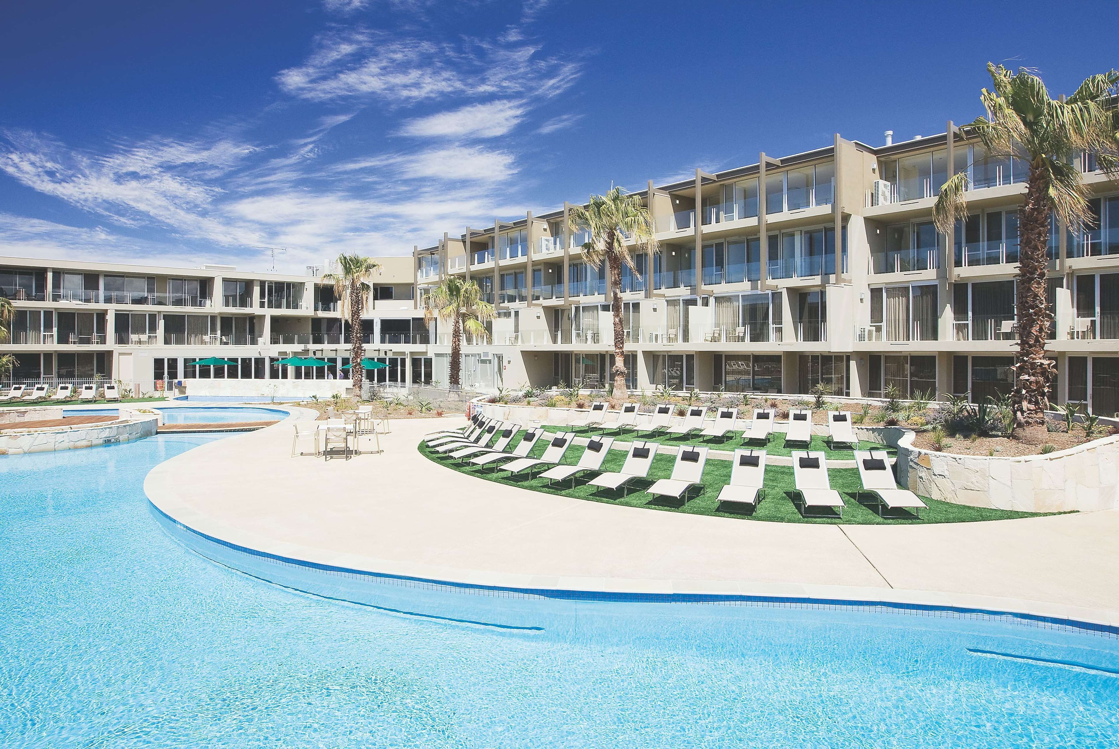 A hotel with a swimming pool, sun loungers, and palm trees.